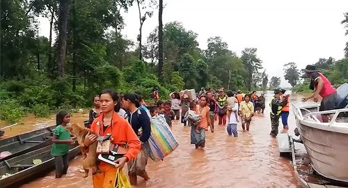 People walk through flooded area after being brought to safety by boat in Sanam Xay district, Attapeu Province, Laos after a hydropower dam under construction in Southern Laos collapsed, in this still picture taken from social media video obtained July 24, 2018.  ATTAPEU TODAY/ via REUTERS  ATTENTION EDITORS - THIS IMAGE HAS BEEN SUPPLIED BY A THIRD PARTY. MANDATORY CREDIT. NO RESALES. NO ARCHIVES. MUST ON SCREEN COURTESY: ATTAPEU TODAY.